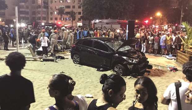 People stand around the car which crashed into people at the Copacabana beach in Rio de Janeiro, Brazil.