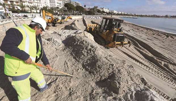 A worker rakes sand as others take part in an operation to enlarge the shoreline of a beach in Cannes.