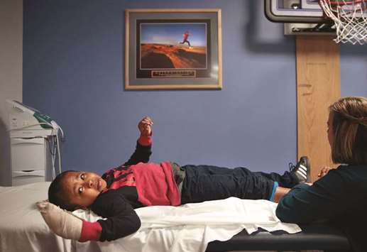 GRIM: Markel Taylor, 6, looks toward his paralysed arm as physical therapist Jackie Patterson stretches the muscles of his right foot at St. Louis Childrenu2019s Hospital. Markel was shot in the head while riding to a football practice session.