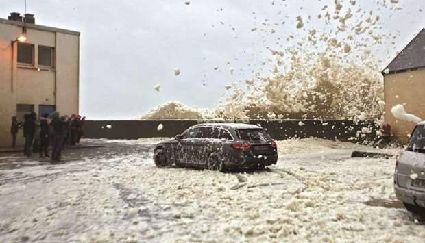 A car drives away from blowing sea foam on the Brittany coast after storm Eleanor hit Saint-Guenole in western France yesterday.