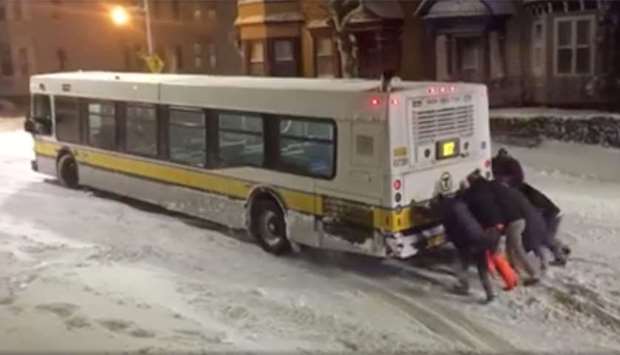 People push a bus on an icy road in Boston, Massachusetts