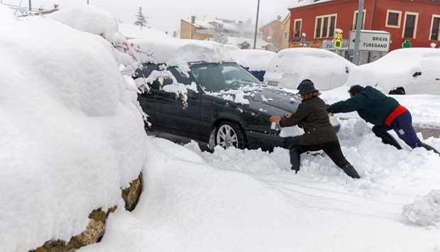 Two people push a snow covered car in Torrecaballeros, Segovia province , Spain