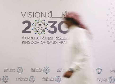 A Saudi man walks past the logo of Vision 2030 in Jeddah (file). The latest handouts will cost the state more than 50bn riyals, Saud al-Qahtani, an adviser to the royal court, said on his Twitter account.