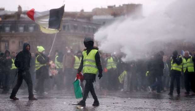 A protester wearing a yellow vest takes part in a demonstration by the ,yellow vests, movement as police use a water cannon near the Arc de Triomphe in Paris.