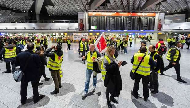 Security staff members wearing vests with the logo of German union verdi stand in front of a board displaying cancelled flights during a strike at the airport in Frankfurt