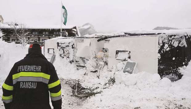 A firefighter is seen near a bus lying on its side after being hit by an avalanche, in the village of Ramsau.