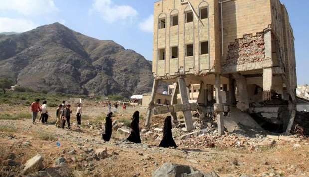 People walk past a school, damaged during the ongoing war in Taiz, Yemen