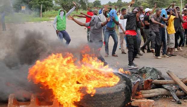 Protesters stand behind a burning barricade during protests on a road leading to Harare, Zimbabwe on Saturday.