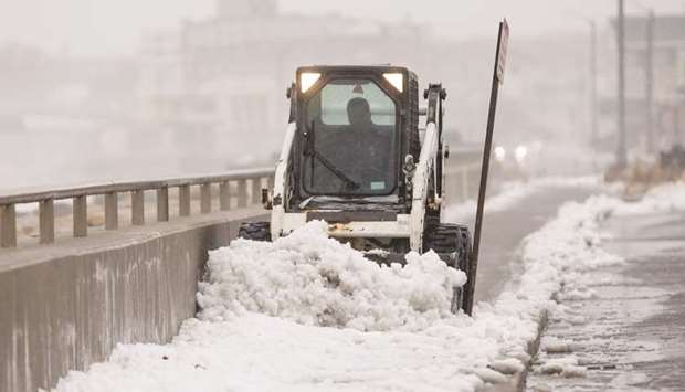 A worker uses a skid loader to clear snow from a sidewalk alongside Nantasket Beach during a winter storm that brought snow, sleet and rain to the area in Hull, Massachusetts.