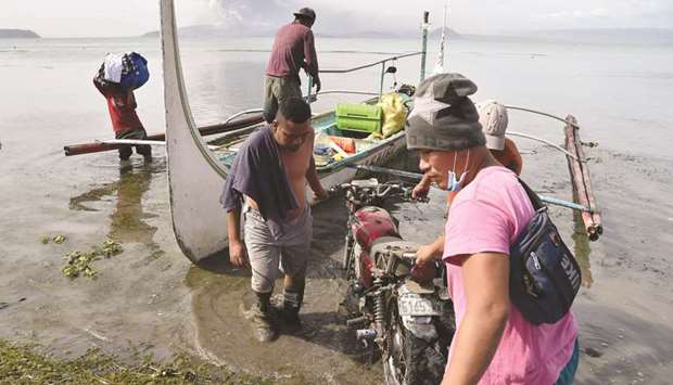 Evacuating residents living at the foot of Taal volcano unload their belongings from an outrigger canoe while the volcano spews ash as seen from Tanauan town in Batangas province, south of Manila, yesterday.