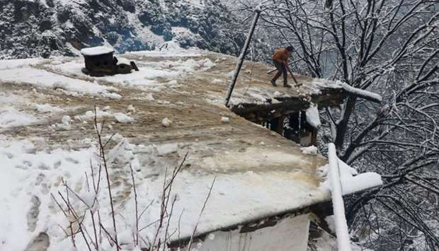A boy clears a snow-covered roof of his family house after a heavy snowfall in Neelum Valley near line of control (LoC), Pakistan, yesterday