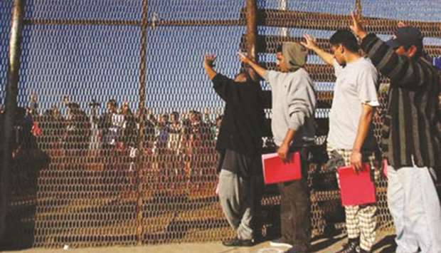 A group of deported immigrants stand near the double steel fence that separates San Diego and Tijuana at the border in Tijuana in this December 10, 2011 file photograph.