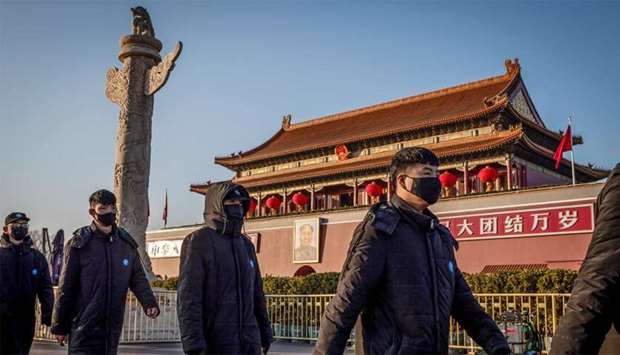 Security personnel wearing protective masks walk in front of the portrait of late communist leader Mao Zedong (C, back) at Tiananmen Gate in Beijing
