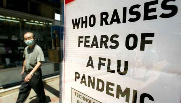 A man wearing a mask to protect against Severe Acute Respiratory Syndrome (SARS) passing a news stand poster saying that the World Health Organisation (WHO) warns that a new influenza pandemic could sweep the globe.
