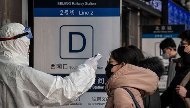 A security personnel wearing protective clothing to help stop the spread of a deadly virus which began in Wuhan, checks the temperature of a woman at a subway station entrance in Beijing