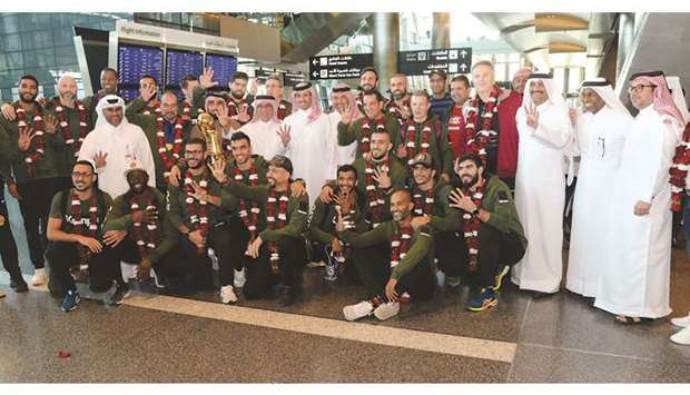 Secretary-General of the QOC Jassim Rashid al-Buenain, Qatar Handball Association president Ahmad al-Shaabi and other officials pose with the Qatar handball team on their arrival in Doha yesterday. At right, coach Valero Rivera, team manager Yusuf al-Hail and player Wajdi Sinan pose with the trophy.