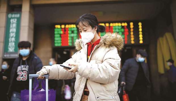 A woman wearing a face mask uses her cellphone as she walks outside Beijing Railway Station as the country is hit by an outbreak of the new coronavirus.