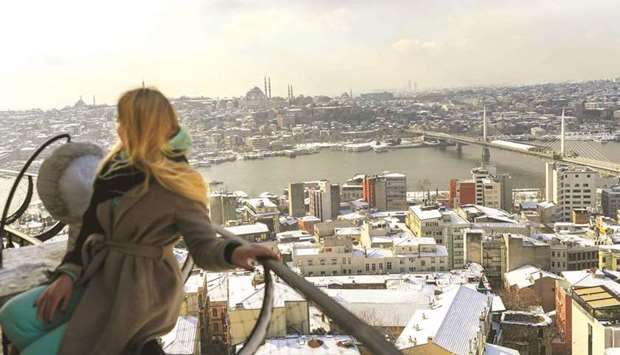 A woman stands on top of the Galata Tower as roofs are covered with snow yesterday in Istanbul. Turkeyu2019s economy will grow 4.0% in 2021, rebounding well from a slump brought on by the coronavirus pandemic, while inflation was seen falling to 11.6% due to tight monetary policy, according to a Reuters poll.