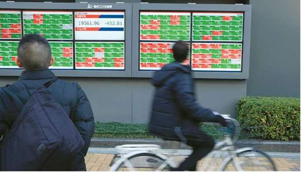 A pedestrian and a man riding his bicycle look at an electronic stock board outside a securities firm in Tokyo. The Nikkei 225 closed 1.4% up at 28,633.46 points yesterday.