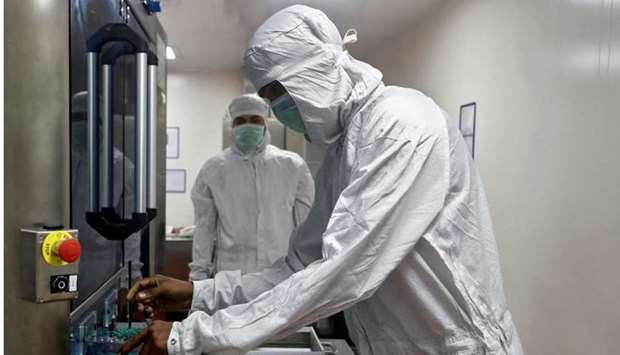 An employee in personal protective equipment removes vials of AstraZeneca's Covishield, coronavirus disease vaccine from a visual inspection machine inside a lab at Serum Institute of India, Pune, India