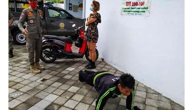 An undated handout picture released by Bali's Satpol PP, the provincial public order agency, shows an official looking on while a man performs push-ups as punishment for not wearing or improperly wearing face masks amid the Covid-19 coronavirus pandemic, along a street in Badung, Indonesia's resort island of Bali.