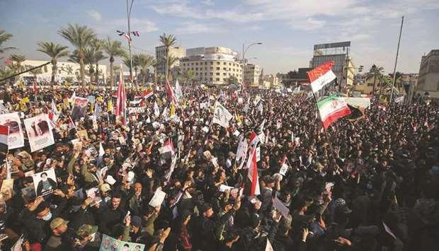 Iraqi demonstrators lift flags and placards as they rally in Tahrir square in the capital Baghdad, yesterday, to mark one year after a US drone strike killed Iranu2019s revered commander Qasem Soleimani and his Iraqi lieutenant Abu Mahdi al-Muhandis near the capital.