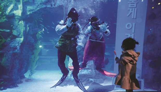 A girl wearing a mask looks at divers in Korean traditional costumes u201cHanboku201d during an event to celebrate New Year amid the coronavirus disease (Covid-19) pandemic at an aquarium in Seoul, yesterday.