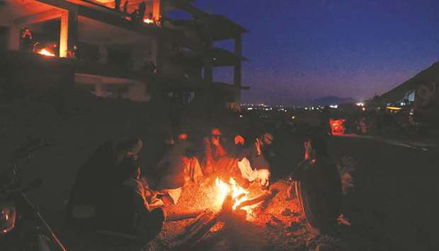 Mourners from the Hazara community warm around a fire near the coffins of miners killed in an attack by gunmen in the mountainous Machh area, during a sit-in protest at the eastern bypass, on the outskirts of Quetta yesterday. 