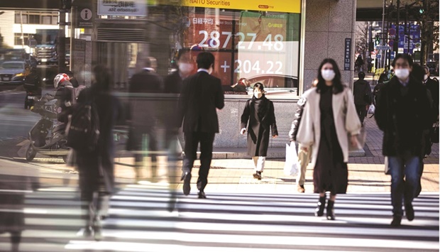 Pedestrians cross a street in front of a stock indicator displaying numbers of Nikkei 225 of the Tokyo Stock Exchange in Tokyo (file). So far this year, Japanu2019s blue-chip index Nikkei 225 has underperformed the Asia benchmark by about three percentage points.