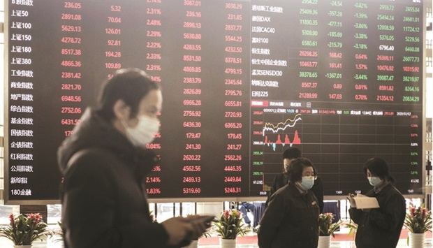 Employees and visitors wearing protective masks walk past an electronic stock board at the Shanghai Stock Exchange. The Composite index closed down 2.6% to 3,433.06 points yesterday.