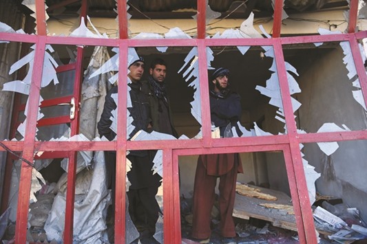 Afghan onlookers watch through the broken windows of a bakery at the site of a suicide car bomb near the international airport  in Kabul yesterday.