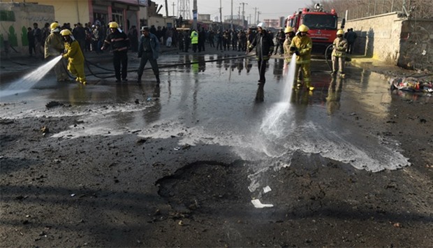 Afghan firefighters use hoses to wash a road at the site of a suicide car bomb near the internationa