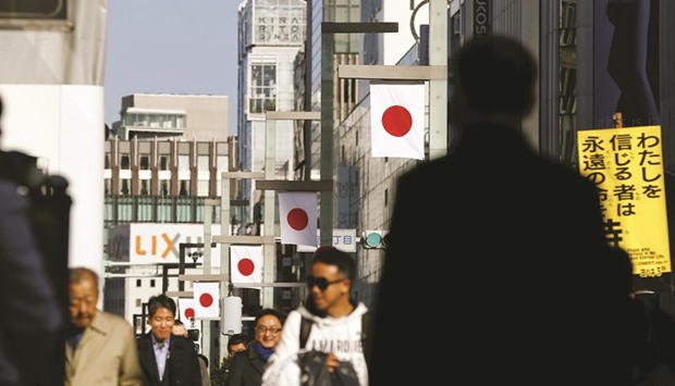 People walk past national flags at a shopping district in Tokyo. Japanu2019s industrial output fell 1.0% in November from the previous month, government data showed yesterday, suggesting that sluggish emerging market demand continues to cloud the outlook for the economy.