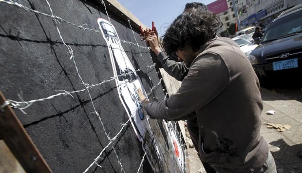 Artist Murad Subai paints graffiti depicting a bottle of water, medicine and a loaf of bread on a street in Sanaa on Thursday. The graffiti is part of a campaign titled ,Wreckage,, which focuses on the issue of the blockade imposed on cities by the war sides and on Yemen by the Saudi-led coalition forces.