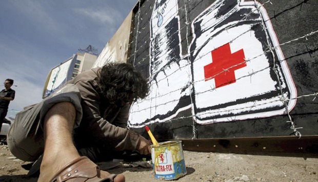 Artist Murad Subai paints graffiti depicting a bottle of water, medicine and a loaf of bread on a street in Sanaa yesterday. The graffiti is part of a campaign titled u201cWreckageu201d, which focuses on the issue of the blockade imposed on cities by the warring sides.