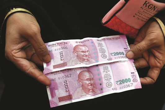 A customer holds new rupee banknotes for a photograph outside an India Post branch in New Delhi. Analysts say the Reserve Bank of India panelu2019s move to hold rates, which caused the benchmark 10-year yield to jump the most since 2013, could revive overseas demand for rupee debt as its yield advantage over Treasuries improves.