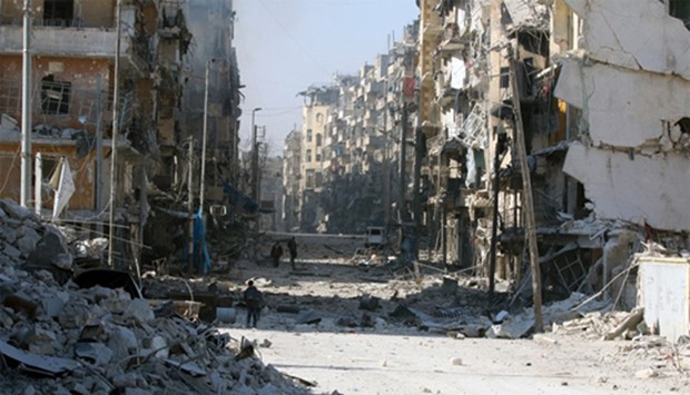 Syrians walk over rubble of damaged buildings, while carrying their belongings
