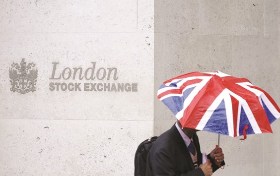 A worker shelters from the rain as he passes the London Stock Exchange building. The FTSE 100 closed up 1.1% to 6,968.57 points yesterday.