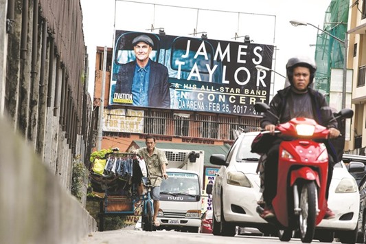 A clothing vendor (left) pedals his bicycle past a billboard promoting a planned concert by US singer James Taylor in Manila yesterday.