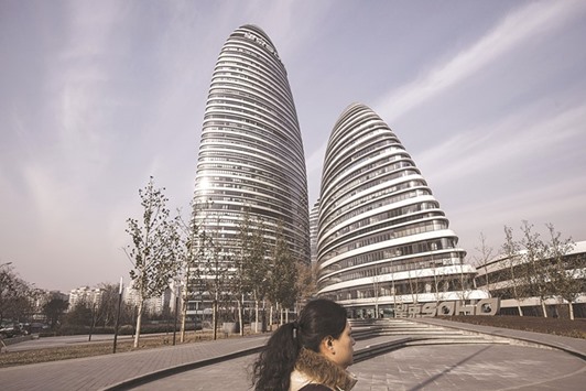 A woman walks past commercial buildings at the Wanjing Soho project in Beijing. The QNB report examines recent developments and the outlook for the Chinese economy as concerns about mounting corporate debt and overheating property prices force the government to scale back stimulus.