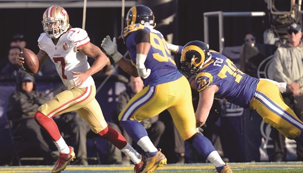 San Francisco 49ers quarterback Colin Kaepernick (L) runs the ball against the defense of Los Angeles Rams defensive end Morgan Fox (R) and defensive tackle Aaron Donald (C) during the second half at Los Angeles Memorial Coliseum.