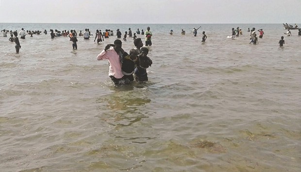 People help a man to come ashore from Lake Albert after at least 30 Ugandan members of a village football team and their fans drowned.