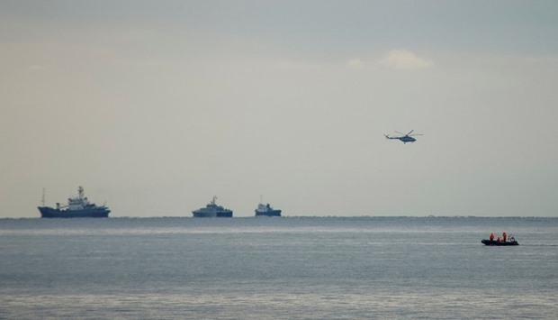 A helicopter flies next to ships at the crash site of a Russian military Tu-154 plane