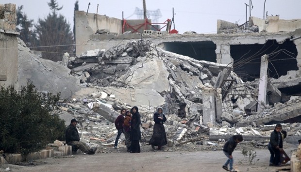 People stand near near rubble of damaged buildings in al-Rai town
