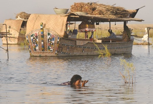 In this photograph taken on September 9, 2016, a woman holds up a plate of food as she makes her way through the water in front of the floating boathouses on Manchar lake.