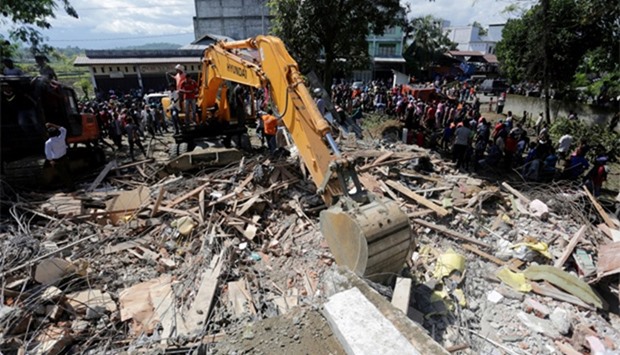 Rescue workers use heavy equipment to search for victims in a collapsed building following an earthquake in Lueng Putu