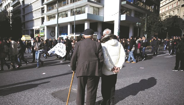 Two elderly men look at protesters marching during a demonstration in Athens marking a 24-hour general strike against labour and tax reforms.