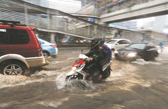 People ride their vehicles through a flooded street at a business district in Jakarta, Indonesia, yesterday.