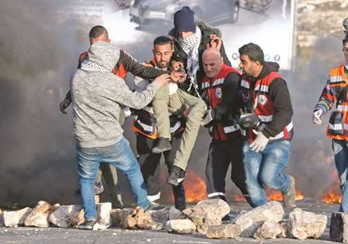 Palestinian paramedic volunteers carry away an injured protester during clashes with Israeli forces in the West Bank city of Ramallah yesterday, as demonstrations continue to flare in the Middle East and elsewhere over US President Donald Trumpu2019s declaration on Jerusalem.
