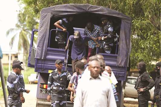 Traders disembark from a police truck after being detained in Libreville, following a knife attack on two Danish nationals.